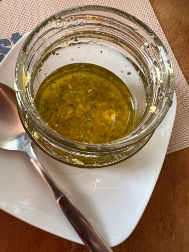 CebollaFlorVinagreta Bote de cristal con ingredientes de vinagreta casera (aceite, lima, mostaza) agitándose para emulsionar.